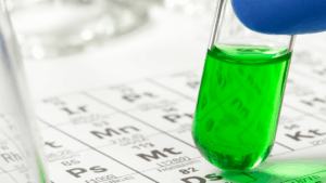 Tubo de ensaio com líquido verde sobre tabela periódica, simbolizando análise de impurezas elementares e segurança farmacêutica conforme ICH Q3D.