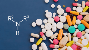 Estrutura molecular genérica de uma nitrosamina (N-N=O com grupos R), sobreposta a uma variedade de pílulas coloridas em um fundo azul, ilustrando a relação entre a química das aminas (incluindo terciárias) e a segurança dos medicamentos.