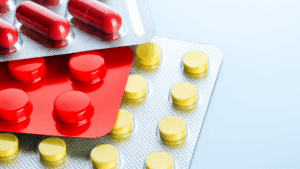 Cientista com luvas verdes inspeciona visualmente frasco de vidro transparente com líquido incolor, etapa inicial em estudos de Extraíveis e Lixiviáveis (E&L) em laboratório farmacêutico.